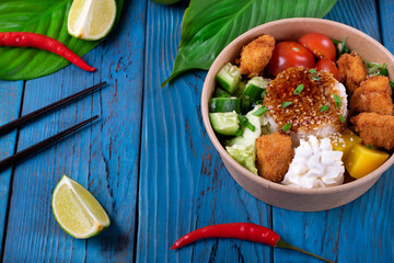 Poke bowl with fried chicken, vegetables and rice on the blue wooden background. Hawaiian cuisine meal