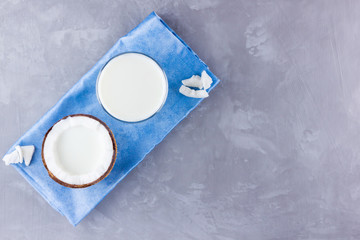 Coconut milk and coconut in glass on gray background. Coconut vegan milk non dairy on blue napkin. Healthy drink concept. Minimalism. Alternative milk. Copy space