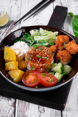 Poke bowl with fried chicken, vegetables and rice on the white wooden table. Hawaiian cuisine meal