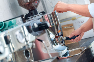 Young adult barista working in coffeeshop, making freshly ground coffee