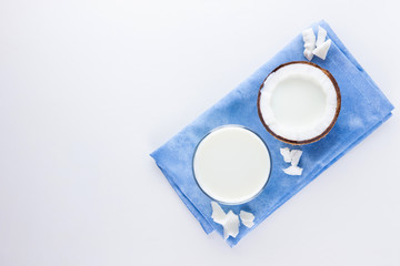 Coconut milk and coconut in glass on white background. Coconut vegan milk non dairy on blue napkin. Healthy drink concept. Minimalism. Alternative milk. Copy space
