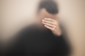 Stressed man covers his face with hand behind glass