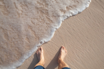 Barefoot male legs stand on wet coastal sand