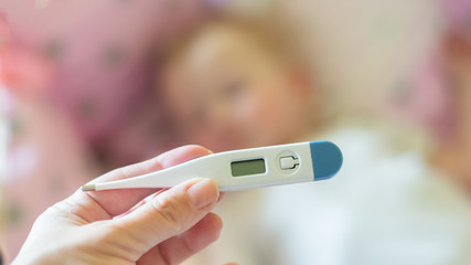 Close-up medical thermometer, Parent measuring temperature of ill kid, 1 years old toddler girl gets high fever lying on bed. fever in child.