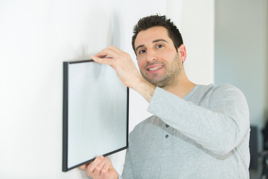 happy man hanging picture frames on wall at home