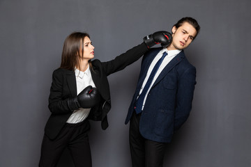 Portrait struggle businessman and business woman with bruises on her arm battle with boxing gloves, isolated on gray background.