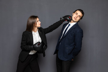 Portrait struggle businessman and business woman with bruises on her arm battle with boxing gloves, isolated on gray background.