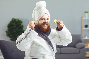 Funny strange fat bearded man with a cosmetic mask on his face in a bathrobe does spa treatments on his face rests in a room at home