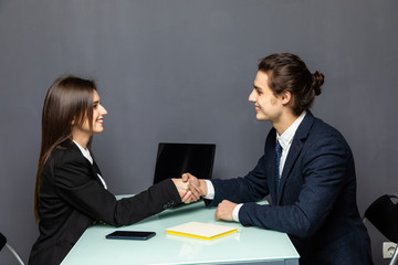 Friendly smiling businessman and businesswoman handshaking over the office desk after pleasant talk and effective negotiation, good relationship, making deal, hiring. Business concept.