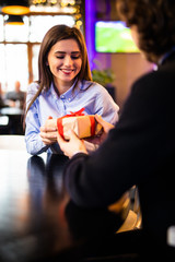 Romantic man giving birthday gift to beautiful emotional woman. Portrait of lovely couple sitting together in cafe, dating. Valentines day concept