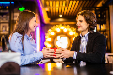 Romantic man giving birthday gift to beautiful emotional woman. Portrait of lovely couple sitting together in cafe, dating. Valentines day concept