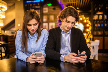 Young couple using mobile smartphones in bar cafe restaurant. Travel people sharing media in social networks with cell phones. Technology addiction concept