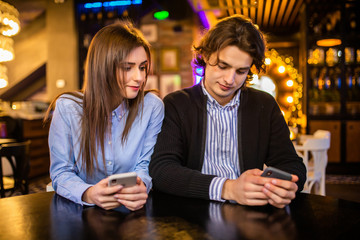 Always connected, internet addiction, young couple in cafe looking at their smartphones, social network concept