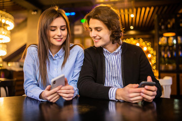 Young couple using mobile smartphones in bar cafe restaurant. Travel people sharing media in social networks with cell phones. Technology addiction concept