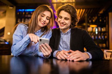 Young in love couple surfing the web or looking at photos on mobile phone in a cafe.