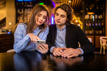 Young in love couple surfing the web or looking at photos on mobile phone in a cafe.