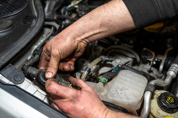 The mechanic bleeds the fuel system with a pump that is on the fuel line, after installing a new fuel filter, the man's hands are visible.