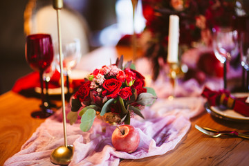 Flowers bouquet of pink, red and white roses in the vase, plate with pomegranates, beautiful candles and invitation cards on the wedding table covered with pink tablecloth