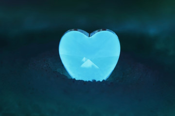 A small heart with a pyramid symbol inside glowing with white-blue light in a pile of sugar. Sweet romantic decor