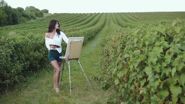 Appealing brunette painting a landscape in windy summer bush field