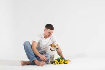 Man and dog with flowers sit on the floor. Romantic Man with bouquet of tulips for birthday. Happy woman's day. Giving bouquet of flowers. Handsome man giving flowers. White background.