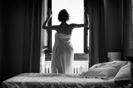 Charming girl stands wrapped in a sheet near a huge window. Back view. The concept of leisure, hotels, travel.