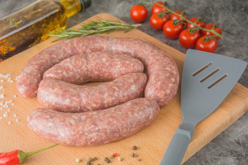 Raw grilled sausages with spices on a worn board.