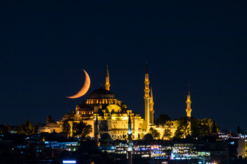 The moon stands like a crescent moon over the Fatih Mosque at night