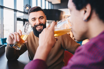 Two male friends enjoying their time in the bar drinking beer and talking.