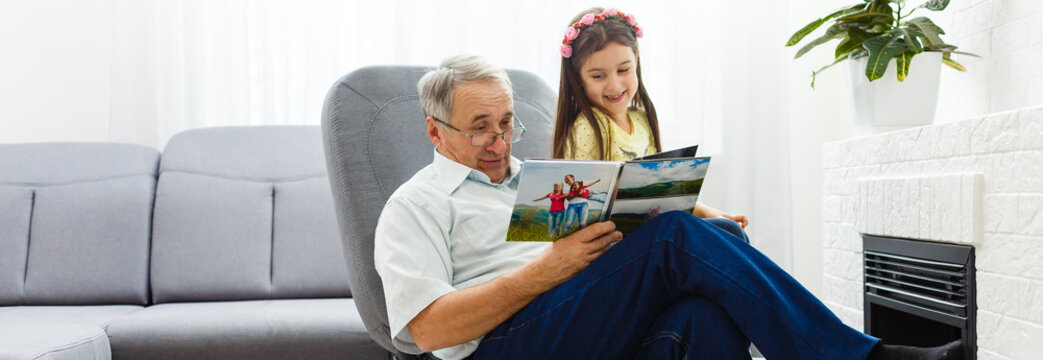 Granddaughter and grandfather watching photos together in a photo album at home