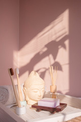 Fototapeta na wymiar White Buddha bust on pastel pink background decorated with shades. Zero waste bamboo toothbrush. Spa asian style. Relax mood. Yoga background. Eco friendly