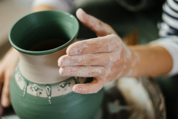 Artist's hand next to painted handmade pot at ceramic workshop.