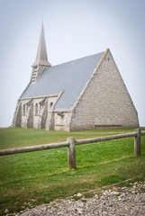 Fototapeta na wymiar Church on the green meadow in the town of Etretat, France. Old beautiful stone Church with a sharp spire.