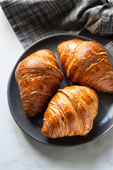 Three delicious fresh croissants on a ceramic plate, light grey background. Top view.