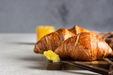 Croissants with jam. Three french croissants on a wooden board and jam on light grey concrete background. 