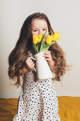 Adorable smiling little girl with yellow tulips.