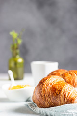 Fresh croissants on a grey linen napkin with jam and coffee. Light grey concrete background. 