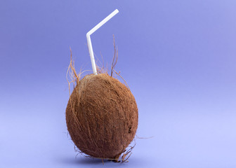 Whole coconut with white straw on purple background.