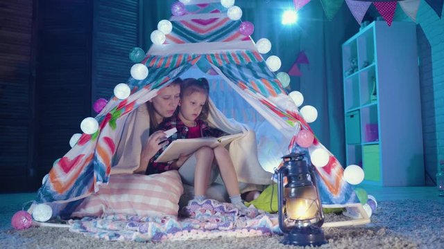 Family Bedtime. Mom And Child Daughter Reading Book In Tent