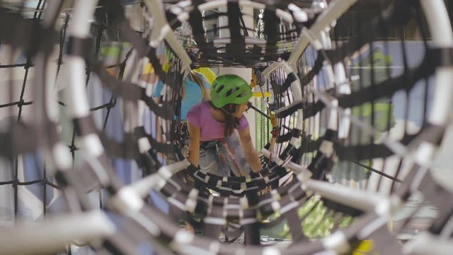 Happy teen girl overcomes obstacles in rope adventure park.