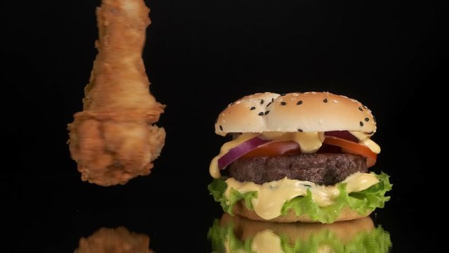 Fried chicken leg rotates next to a burger on a black background.