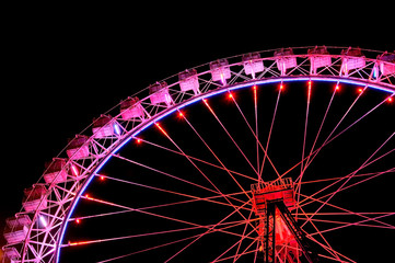 Big ferris wheel with festive red illumination against night sky