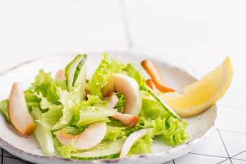 plate of salad with seafood and olives on a light background of boards.