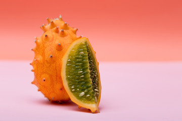 One orange Kiwano and half Kinavo on a pink and orange background.