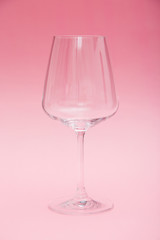 Empty wine glass which stands on a pink background.
