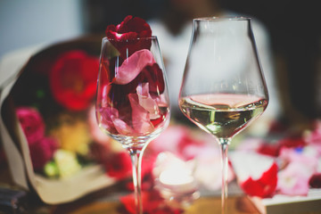 Beautiful glass with rose leafs, rose-petal, rose petals on a romantic date with wine, candles in candlelight and with celebrating couple on the background, interior for a romantic date diner