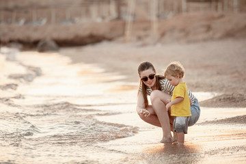 Fototapeta premium Happy mother and toddler play on the seaside. Mom and baby play in the sea beach. Mother's love. Lifestyle. Summer rest. Family vacation. Mothers day.