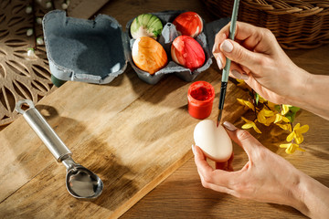 Hands painting Easter eggs on wooden table during spring time
