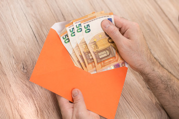 Męska dłoń trzyma kopertę i wyjmuje z niej banknoty Euro o nominałach 50 Euro.