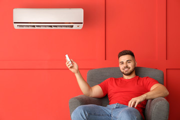 Young man switching on air conditioner at home